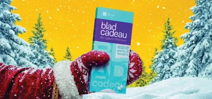 Hand van de kerstman tegen een gele achtergrond met een Bladcadeau in de hand en besneeuwde bomen