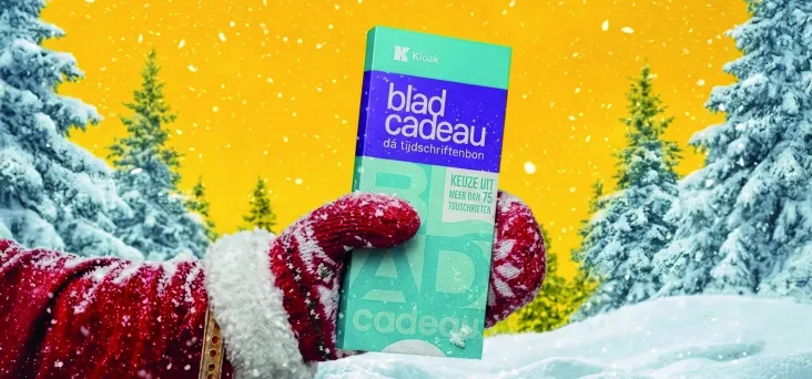 Hand van de kerstman tegen een gele achtergrond met een Bladcadeau in de hand en besneeuwde bomen