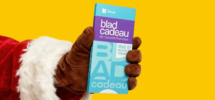 Hand van de kerstman tegen een gele achtergrond met een Bladcadeau in de hand en besneeuwde bomen